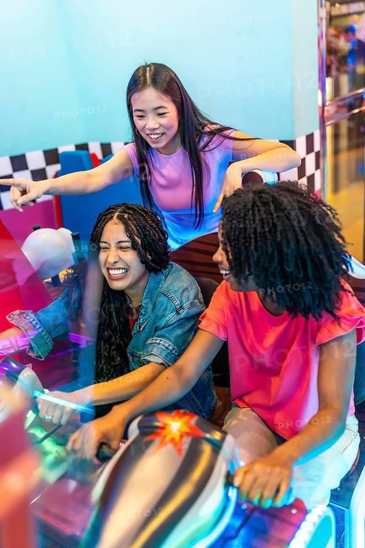 Group of female friends enjoying a lively gaming session, laughing and competing in a racing game at an exciting entertainment venue