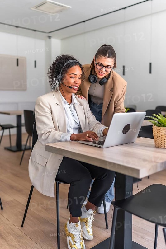 Two female customer service representatives collaborating on a laptop, providing assistance and solutions in a contemporary workspace