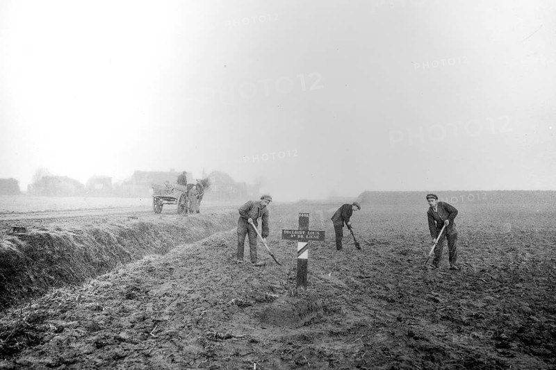 Wooden cross on grave of fallen soldier and workers levelling field on former battlefield after the First World War One in West Flanders, Belgium