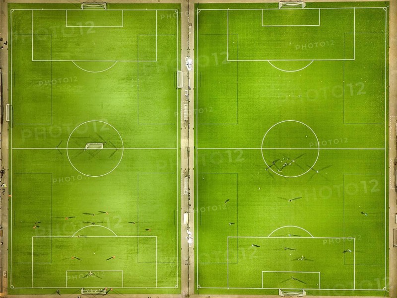 Two symmetrical football pitches from a bird's eye view with scattered players on the green pitch