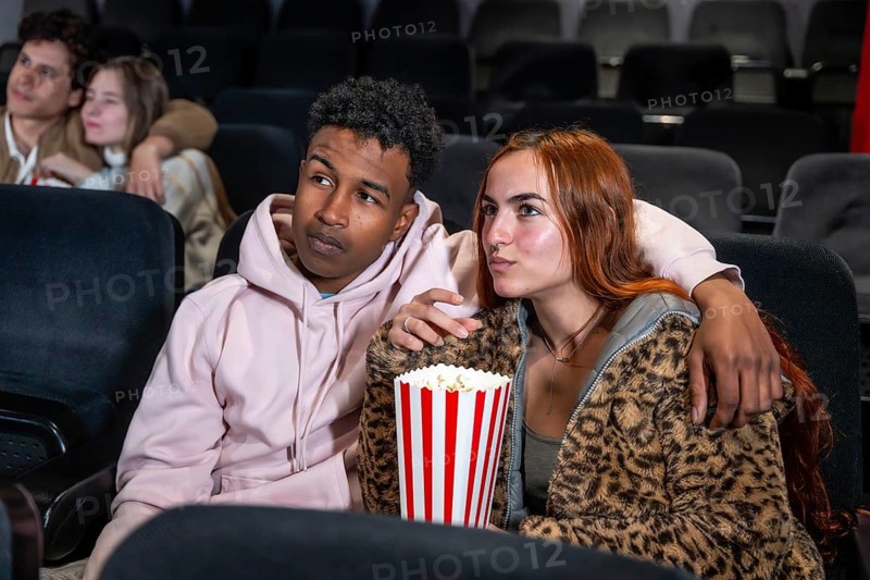 Young multi ethnic couple watching a movie in cinema, eating popcorn and enjoying their time together
