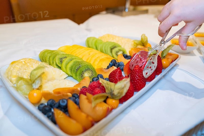 A fruit plate with various fresh fruits, a hand helps itself with tongs, Europäischer Hof, Königsbach Stein, Germany