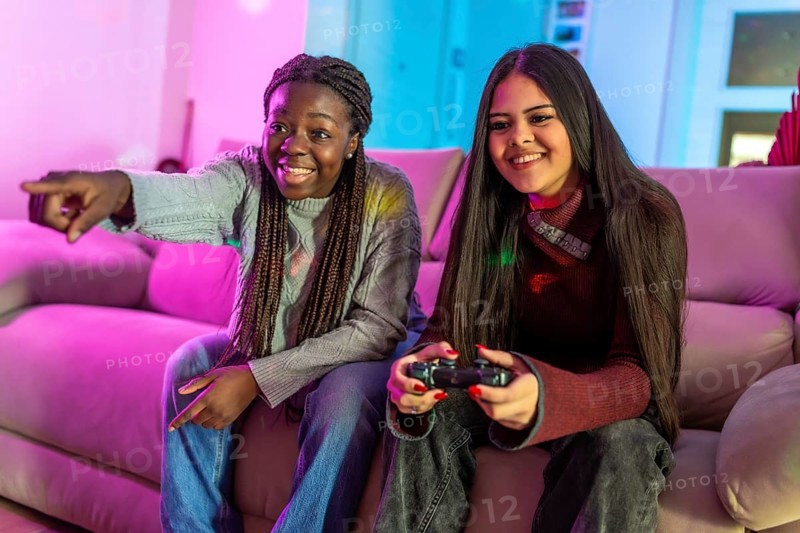 Two friends enjoying their free time playing video games at home, sitting on a comfortable sofa in a colorful living room