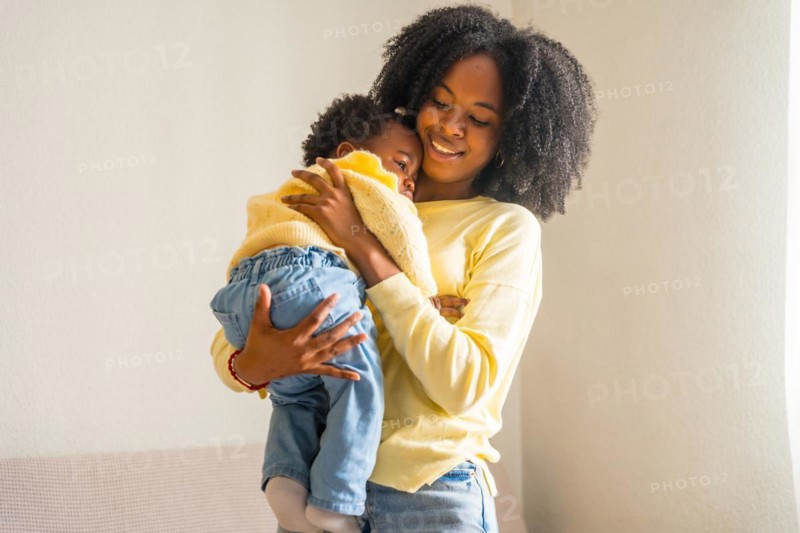 African mother holding her little daughter in arms standing at home