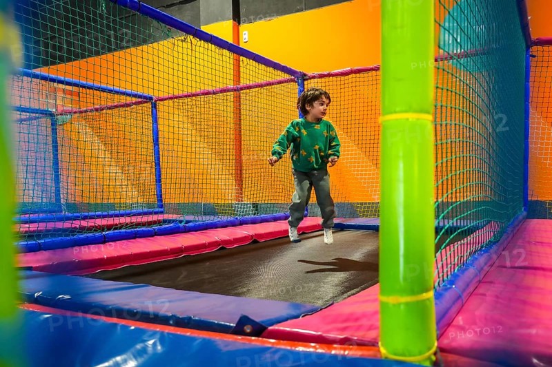 Young boy enjoying playtime, bouncing on a trampoline inside a vibrant and safe indoor play area