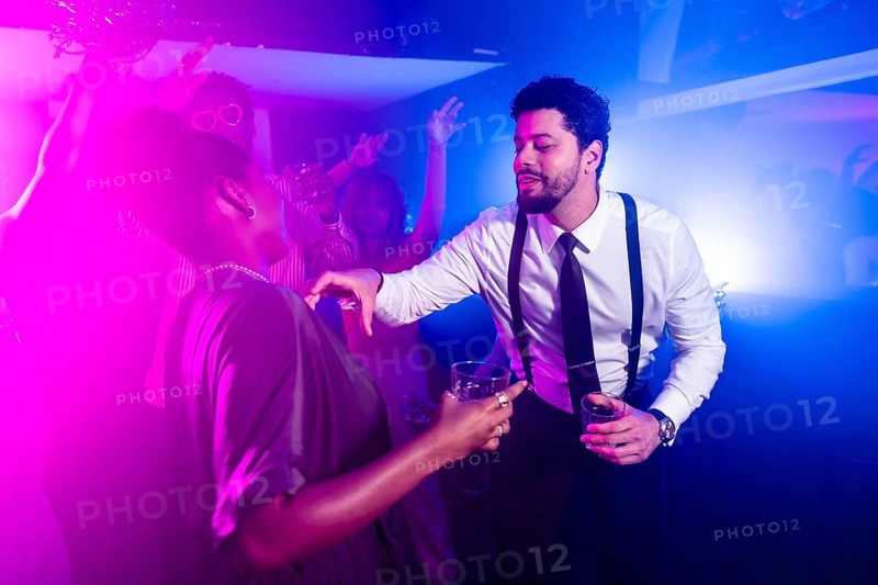 Businessman flirting with beautiful woman while holding alcoholic beverages and dancing at nightclub party with friends in background