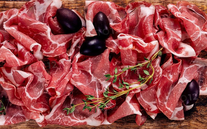 Freshly cut dried meat, served with olives and herbs, on a wooden chopping board, no people