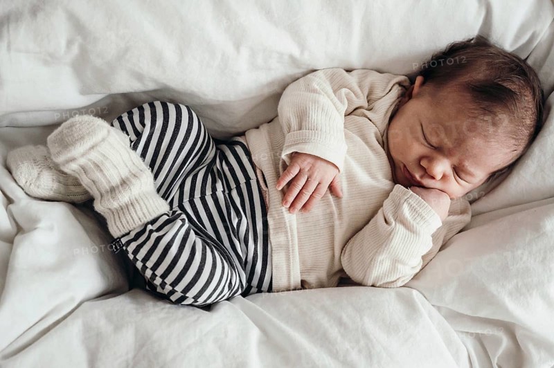 Sleeping baby in a striped romper lying on a white bed, looks peaceful and secure