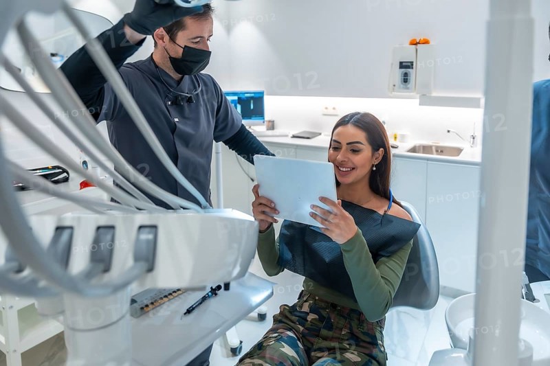 Dentist showing dental scan results on a tablet to smiling patient, in a modern dental clinic