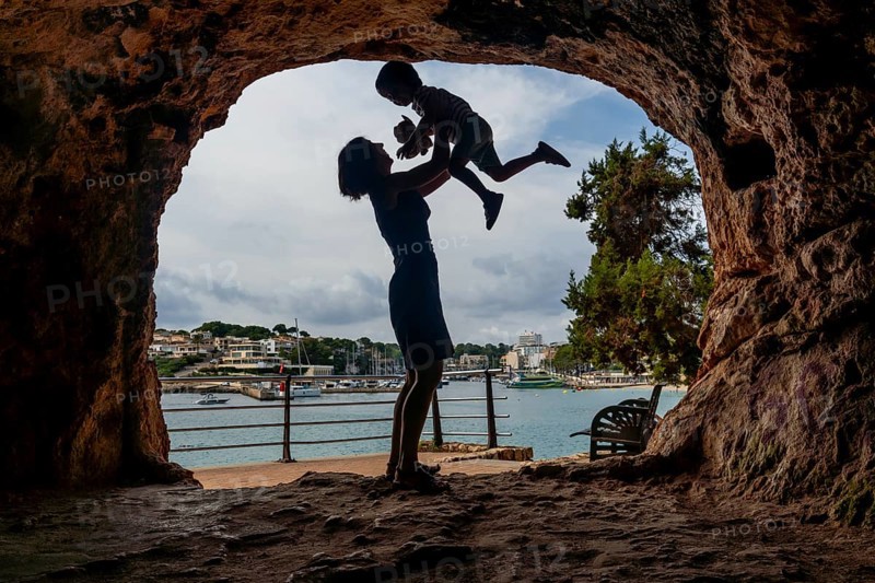 Silhouette of a mother lifting her son inside a cave with a view of the harbor in puerto cristo, mallorca, spain