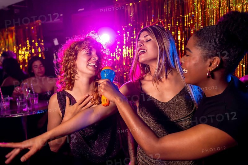 Group of female friends enjoying karaoke night, singing with passion and having fun together in vibrant nightclub atmosphere