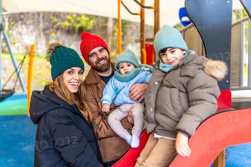 Smiling family bundled in winter clothes, enjoying quality time together while playing on a colorful playground slide in the park