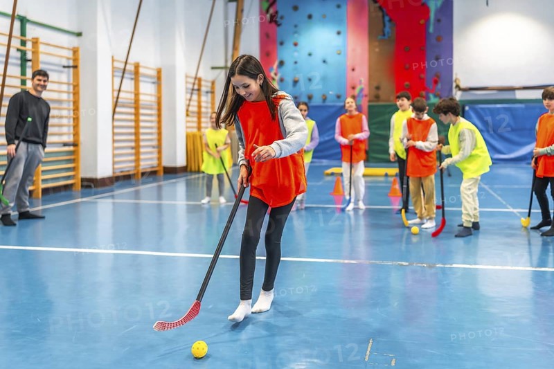 Elementary school students learning and playing floorball in a gym class with their teacher