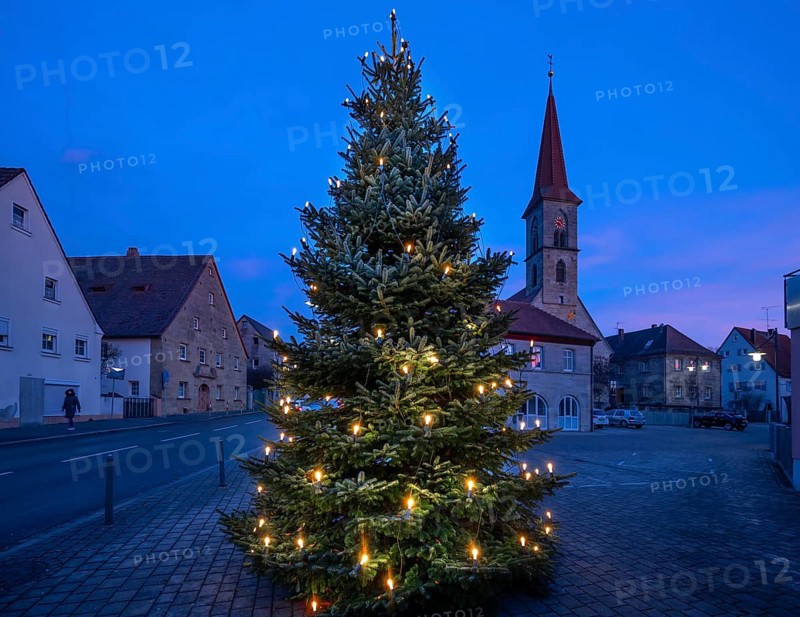 Illuminated Christmas tree on the village square at dusk, St Bartholomew's Church in the background, Eschenau, Middle Franconia, Bavaria, Germany
