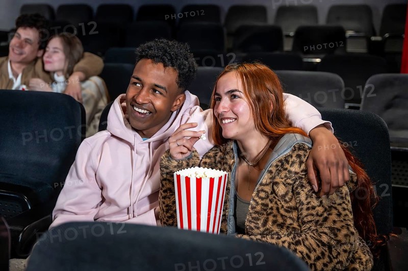 Happy couple sharing popcorn while watching a movie at the cinema, enjoying a night out with friends