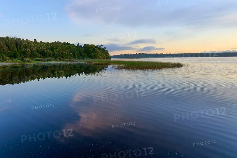 A calm lake in the morning with peaceful natural scenery and reflective clouds, Lake Mahinapua, Ruatapu, South Island, New Zealand