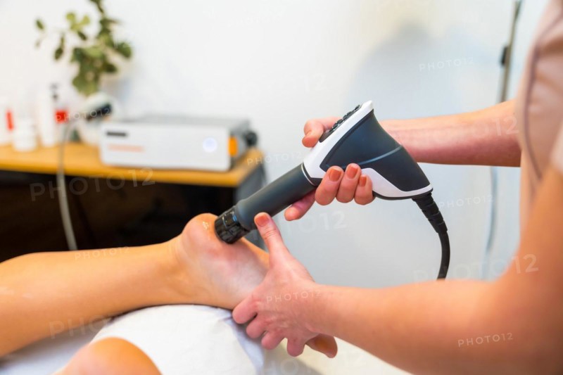 Close-up of an unrecognizable patient on stretcher receiving a shockwave therapy massage on foot in a holistic clinic
