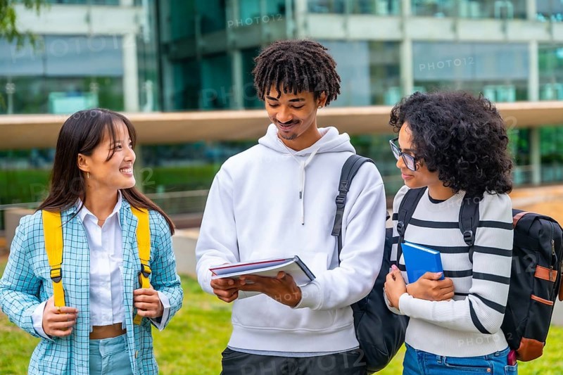 Happy multi-ethnic university students reading notes together standing outside the university in a modern and green campus