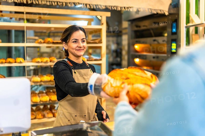 Latin smiling woman selling bread to a client in an artisan bakery