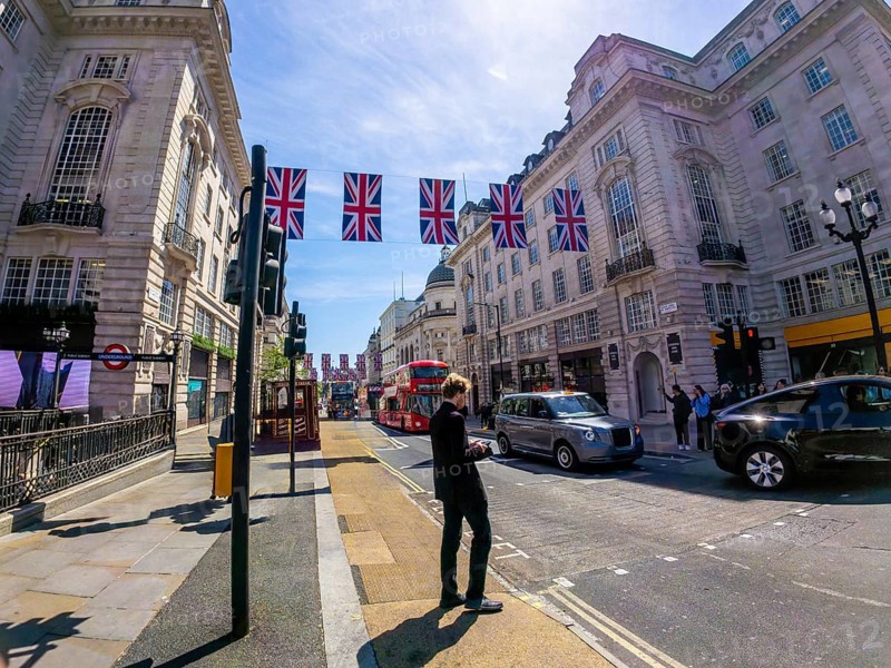 Businessman using smartphone on a london street decorated with british flags, with typical red bus and black cab in the background
