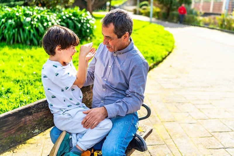 Grandfather and grandson enjoying a playful moment together, sitting on a park bench surrounded by greenery