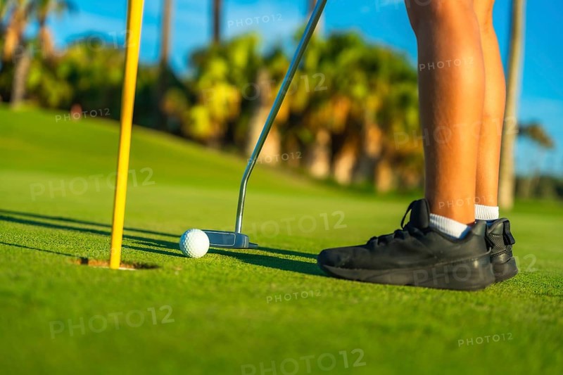 Person putting golf ball in a green course, low section