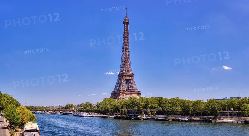The Eiffel Tower from afar with a river and green treetops on a sunny day, Paris