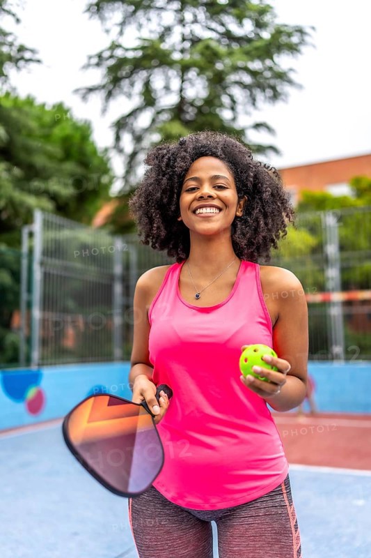 Vertical portrait of a latin female pickelball player standing smiling at camera in an outdoor court