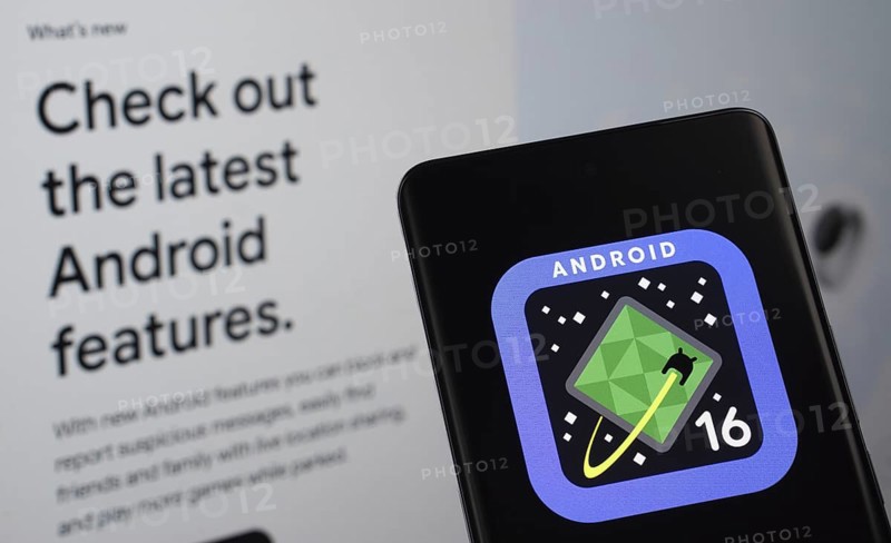 The logo of the Android 16 is displayed on a smartphone screen, with the android website visible on a computer screen in the background