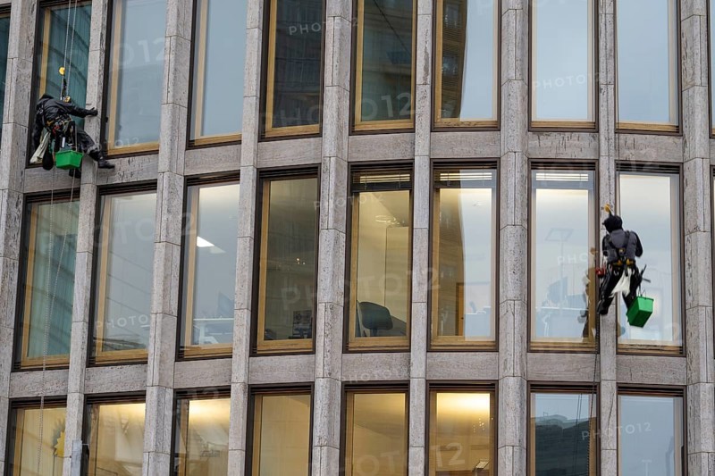 Window cleaners hanging on the facade of a commercial building, Potsdamer Platz, Berlin, Germany