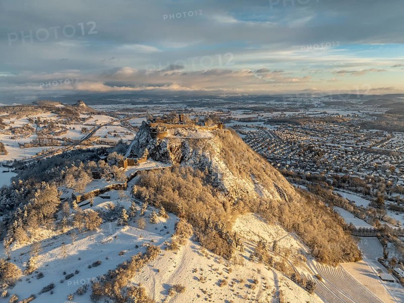 Aerial view of the snow-covered Hegau volcano Hohentwiel with Germany's largest castle ruins on a cold winter morning, at sunrise, on the right the town of Singen, on the left on the horizon the neighbouring Hegau volcano Hohenkrähen, district of Constance, Baden-Württemberg, Germany