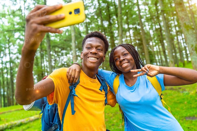 Cheerful african friends taking selfie gesturing victory with hand while hiking in the forest