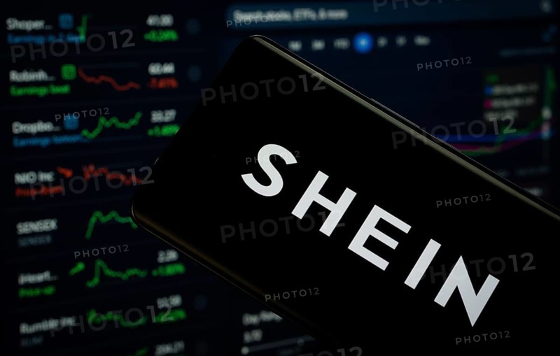 Dhaka, Bangladesh- 18 March 2025: shein logo is displayed on a smartphone screen, with a stock graph webpage visible on a computer screen in the background