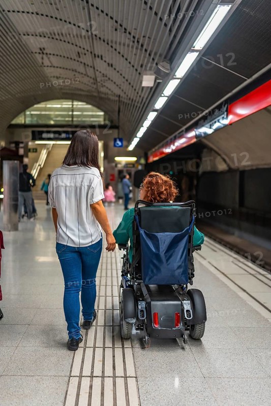 Rear view of a disabled woman and caregiver in the platform of the metro
