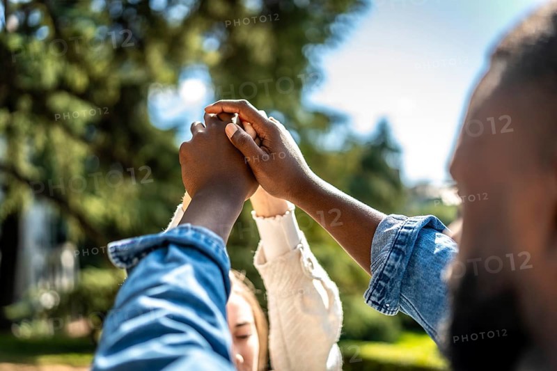 Multi-ethnic couple holding hands and raising them in a park