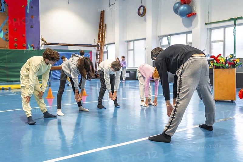 Teenagers bending forward and touching toes while exercising together in school gym class