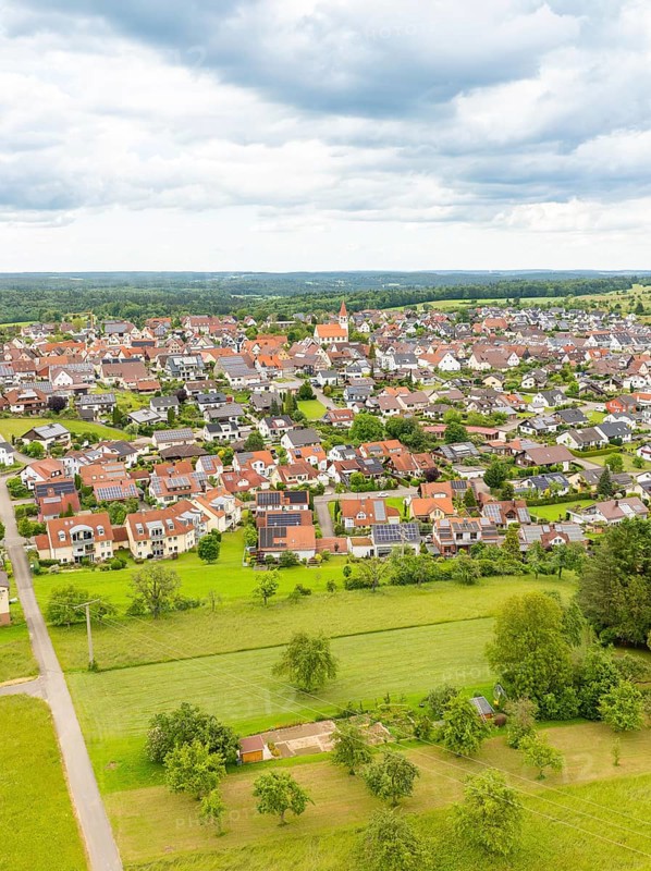 Aerial view of a village with red roofs, surrounded by green meadows and trees under a cloudy sky, Deckenpfronn, Black Forest, Germany