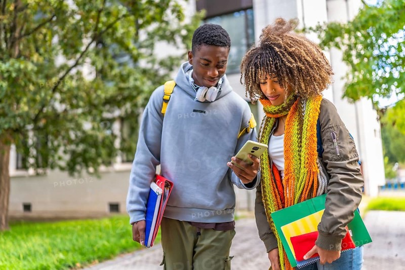 Multiracial college student walking out of class while looking at mobile phone