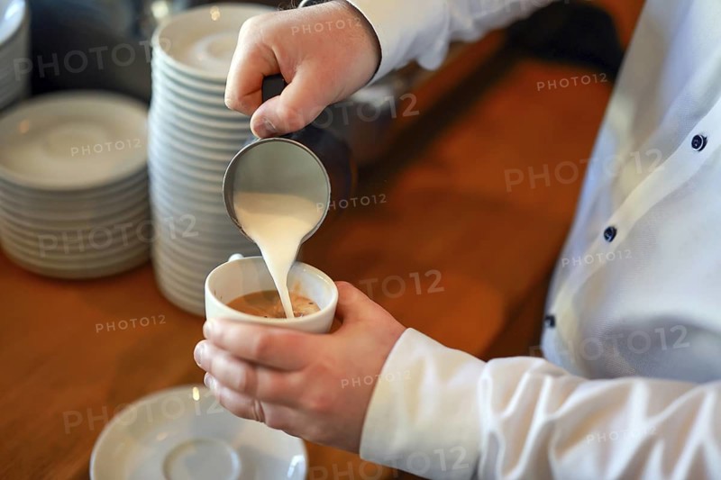 Germany - Barista prepares a coffee, here a cappuccino, hand pours milk foam from a pot into a cup with espresso coffee