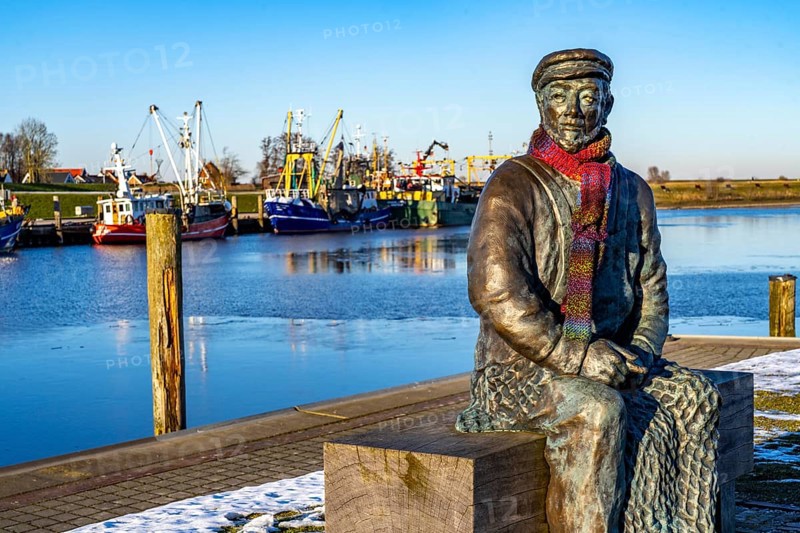 The fishing village of Greetsiel, historic fishing harbour, with the largest shrimp cutter fleet in East Frisia, historic houses, sculpture The Net Maker, winter, partly frozen, in Lower Saxony, Germany