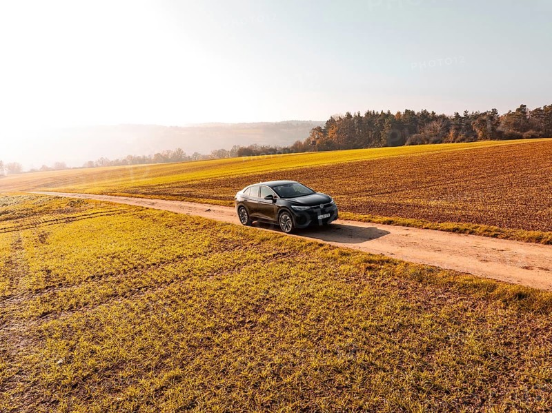 A black car on a dirt road in the middle of golden autumnal fields in sunlight, electric car VW ID5, Deer Carsharing, Gechingen, Black Forest, Germany
