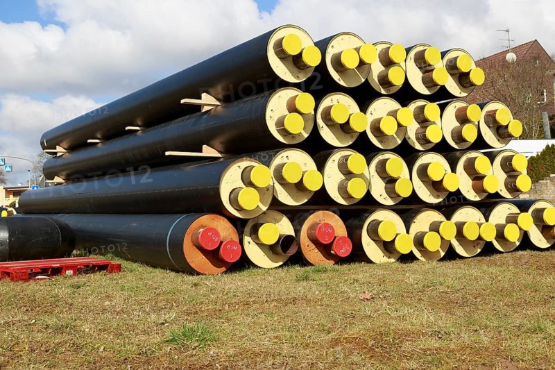 Stacked district heating pipes and district heating lines with yellow ends lie piled up in a meadow