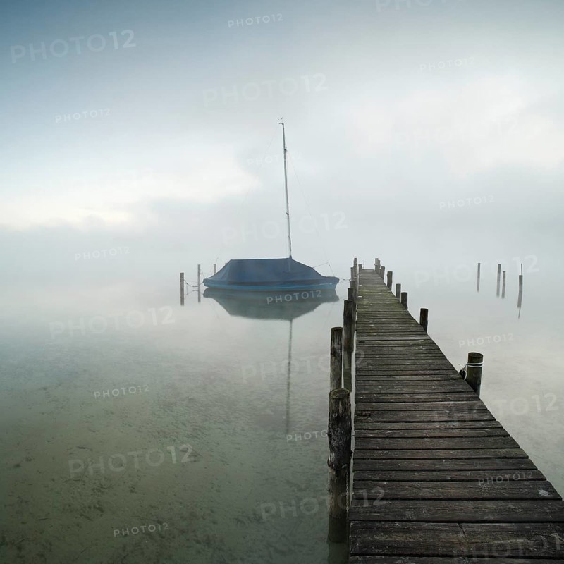 Quiet autumn morning on Lake Chiemsee, jetty with sailing boat in dense fog, Prien am Chiemsee, Bavaria, Germany