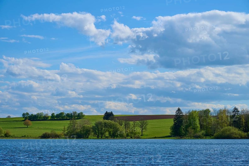 Ober- Moosersee surrounded by green fields and trees under a partly cloudy blue sky, spring, Freiensteinau, Vogelsberg, Hesse, Germany