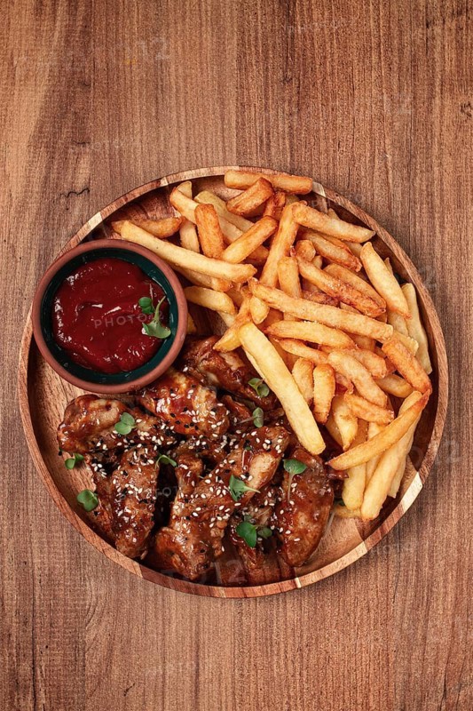 Barbecue chicken wings, sprinkled with sesame seeds, with French fries, and sauce, on a wooden plate, rustic style