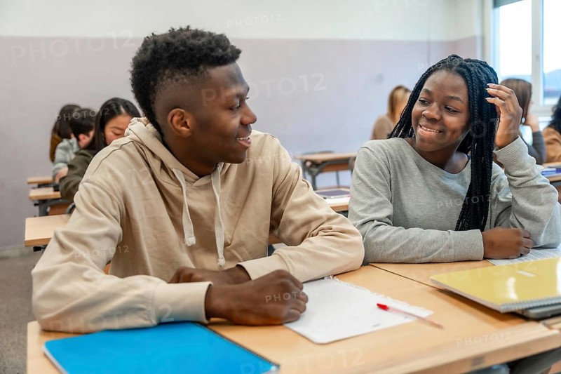 Two college students smiling and engaging in conversation during a lesson, enjoying their time together in a vibrant classroom setting