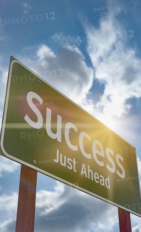 Success just ahead green road sign against a blue sky and clouds