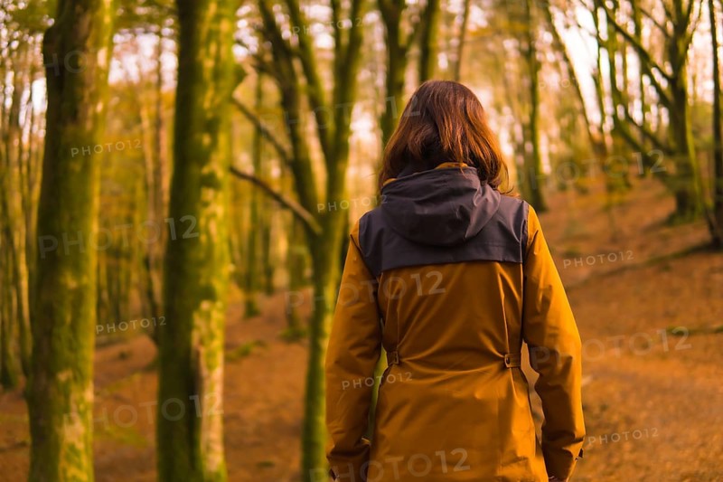 Lifestyle, a young woman in a yellow jacket walking backwards along a forest path in autumn. Artikutza Forest in San Sebastián, Gipuzkoa, Basque Country. Spain