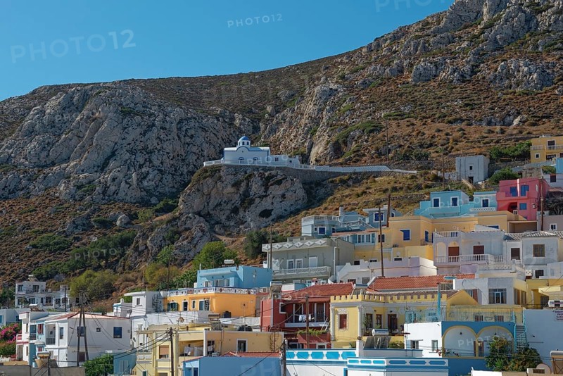 Colourful houses of Menetes with the chapel of Agios Spiridonas on a rock in front of a hill, Menetes, Karpathos, Greece
