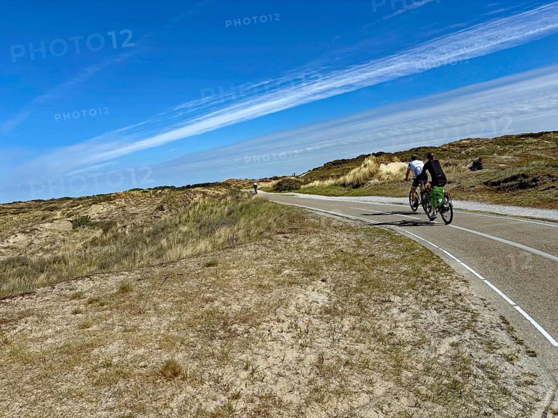 Cyclist on a wide cycle path through a dune landscape under a blue sky with clouds, north sea Cyle route, Scheveningen, Netherlands